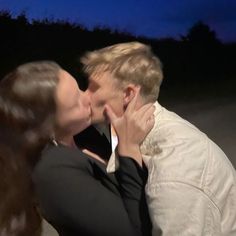 a man and woman kissing each other in front of a dark blue sky at night