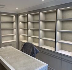 an empty room with white shelves and grey counter tops in front of the door to another room