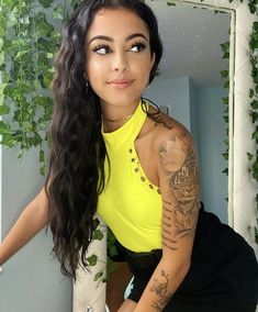 a woman in yellow shirt and black skirt with tattoos on her arm posing for the camera