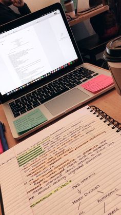 an open laptop computer sitting on top of a wooden desk next to a cup of coffee