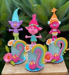 three colorful figurines sitting on top of a wooden table in front of plants