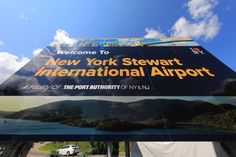 a sign for the new york stewart international airport in front of a blue sky with clouds