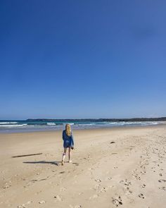 a woman is walking on the beach near the ocean