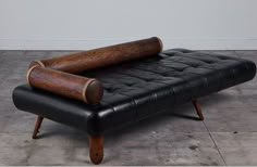 a black leather couch with wooden legs and a rolled up pillow on it's back