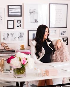 a woman sitting at a desk in front of pictures on the wall behind her and holding a pink teddy bear