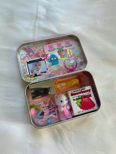 two tins with toys in them sitting on a white bed sheet, one opened and the other closed