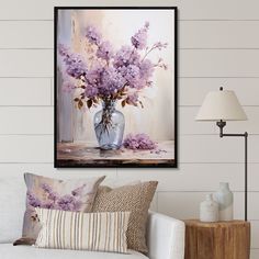 purple flowers in a vase on a table next to a white couch with pillows and lamps