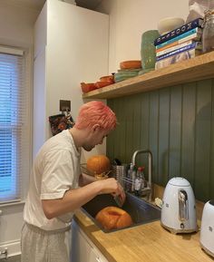 a man with pink hair washing bread in a kitchen sink