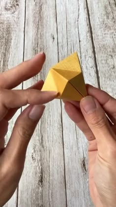 two hands holding an origami piece on top of a wooden table next to each other