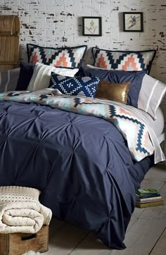 a bed with blue comforter and pillows on top of it in front of a brick wall