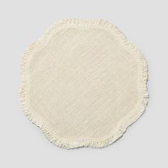 a white round rug with fringes on the bottom and side, in front of a gray background