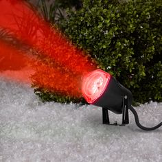 a red light is on top of a black object in the snow near some bushes