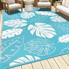 a blue and white area rug on a wooden deck with two chairs, an umbrella and potted plants in the background