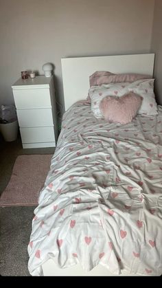 a bed with pink hearts on it in a room next to a white dresser and nightstand