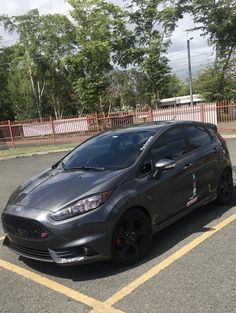 a grey car parked in a parking lot next to a red fence and some trees