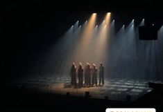 a group of people standing on top of a stage in front of spotlights at night