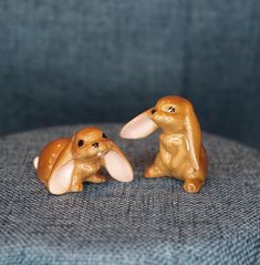 two small figurines of rabbits sitting on a blue chair with their backs to each other