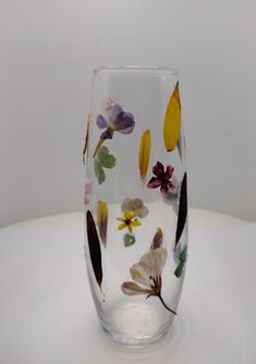 a glass with flowers painted on it sitting on top of a white tableclothed surface