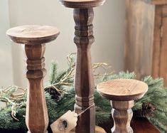 three wooden candlesticks sitting on top of a table next to pine cones and evergreen branches