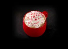 a red mug filled with whipped cream and sprinkles on a black background