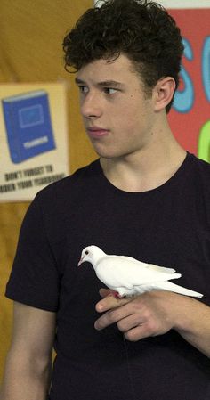 a young man holding a white bird in his right hand and wearing a black shirt