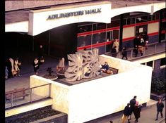 people are walking around in front of a building with an artistic sculpture on the outside