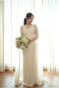 a woman standing in front of a window holding a bouquet of flowers and wearing a wedding dress