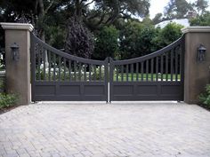 an iron gate and brick walkway leading to a driveway