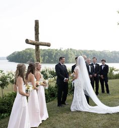 a bride and groom standing in front of a cross with their wedding party looking on