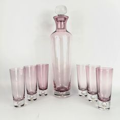 a pink vase and six glasses on a white table