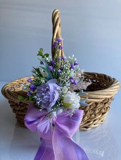 a basket filled with purple and white flowers next to a ribbon tied around the handle