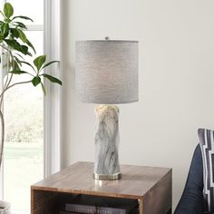 a table with a lamp on it next to a book shelf and a couch in front of a window