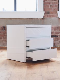 a white dresser sitting on top of a hard wood floor next to a brick wall