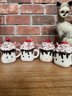 four coffee mugs with chocolate frosting and cherries on them are lined up in front of a brick wall