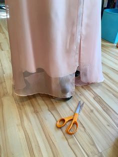 a pair of scissors sitting on top of a wooden floor next to a pink curtain