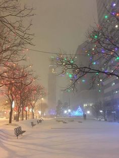 a city street covered in snow with christmas lights on trees and people walking down the sidewalk