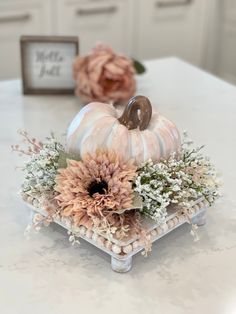 a white and pink pumpkin centerpiece sitting on top of a table with flowers in it