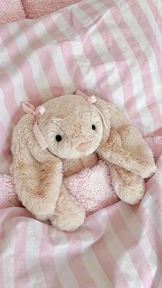 a teddy bear sitting on top of a pink and white striped comforter in a bed