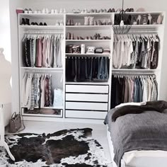 a white closet with clothes and shoes on shelves next to a black cowhide rug