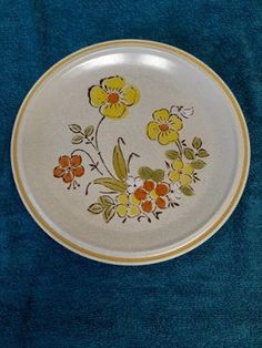 a white plate with yellow and orange flowers painted on the side sitting on a blue surface