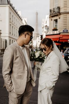 a man and woman standing next to each other in front of a building with flowers