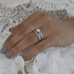 a woman's hand with two wedding rings on top of her finger and white flowers in the background