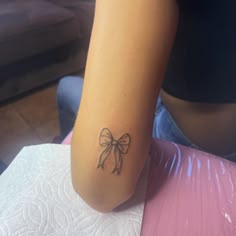 a woman with a bow tattoo on her left arm, sitting in front of a chair