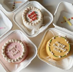 four decorated birthday cakes sitting in small trays on a white table top, with the words happy birthday written on them