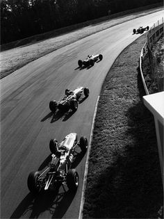 three race cars racing down a track in the middle of an open air course, with one being pushed by another car