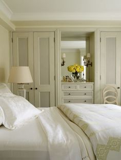 a bedroom with white furniture and yellow flowers in the vase on the dresser next to the bed