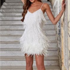 a woman wearing a white feather dress standing in front of stairs with her hand on her head