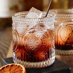 two glasses filled with liquid sitting on top of a wooden table next to an orange slice