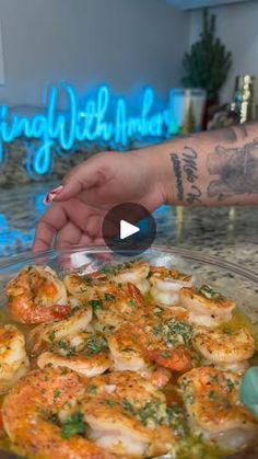 a person holding onto a plate with shrimp in sauce on the counter next to a neon sign