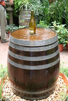 a bottle of wine is sitting on top of a barrel in the middle of a garden